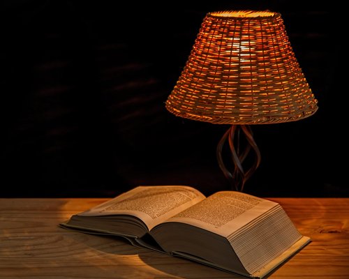 Book on a desk with a warm reading lamp nearby